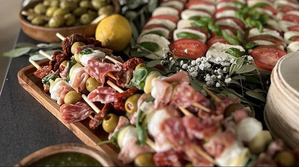 Langes Buffet: Caprese mit Basilikum, Antipasti-Spieße mit Salami und Oliven, dazu eine Schale grüner Oliven
