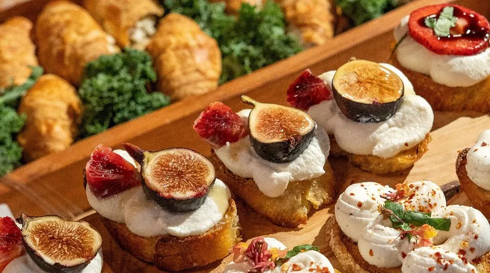 Crostini mit Frischkäse, frischer Feige und getrockneter Tomate auf einem Holzbrett